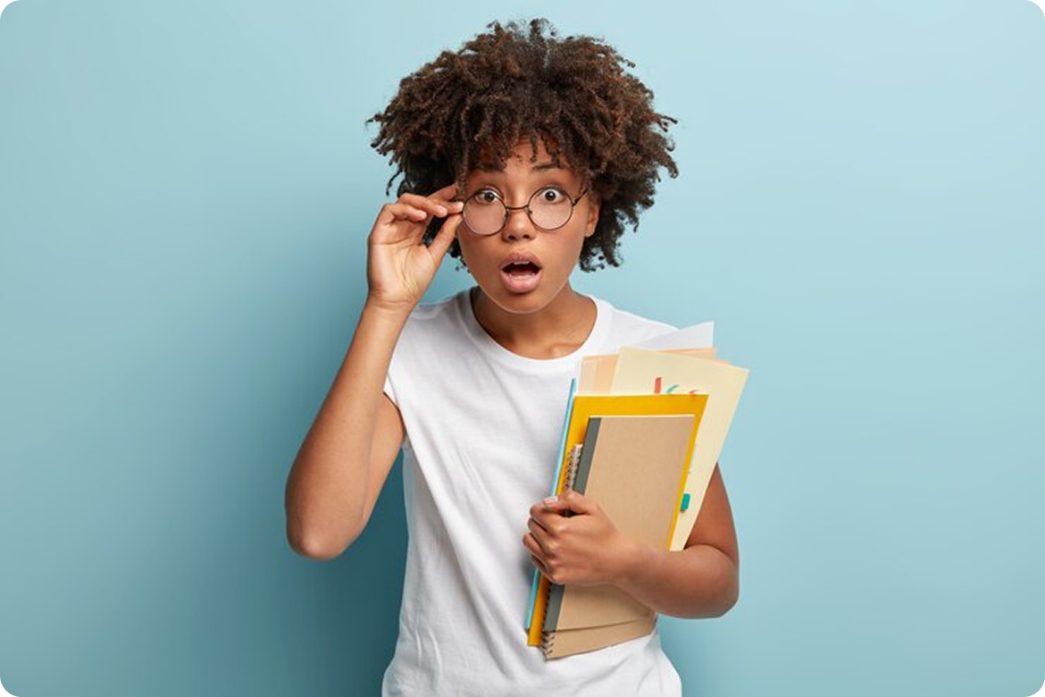 Jovem negra de óculos com expressão de surpresa segurando livros e cadernos
