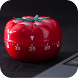 Cronômetro em formato de tomate (Pomodoro) sobre uma mesa de estudos, representando técnicas de gestão de tempo e produtividade