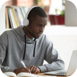 Jovem negro focado estudando em um laptop com fones de ouvido e fazendo anotações