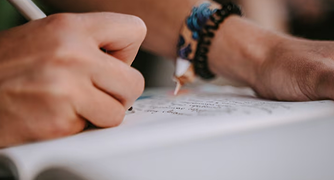 Close detalhado das mãos de um estudante escrevendo em um caderno com uma caneta branca
