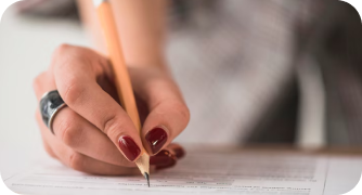 Close das mãos de uma pessoa com unhas pintadas de vermelho segurando um lápis e preenchendo cuidadosamente uma folha de respostas ou formulário